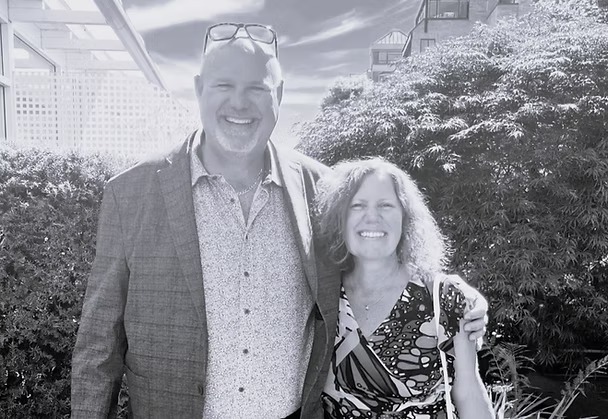 Smiling couple outdoors with trees and buildings.