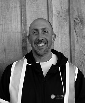 Smiling person wearing safety vest in front of wood.