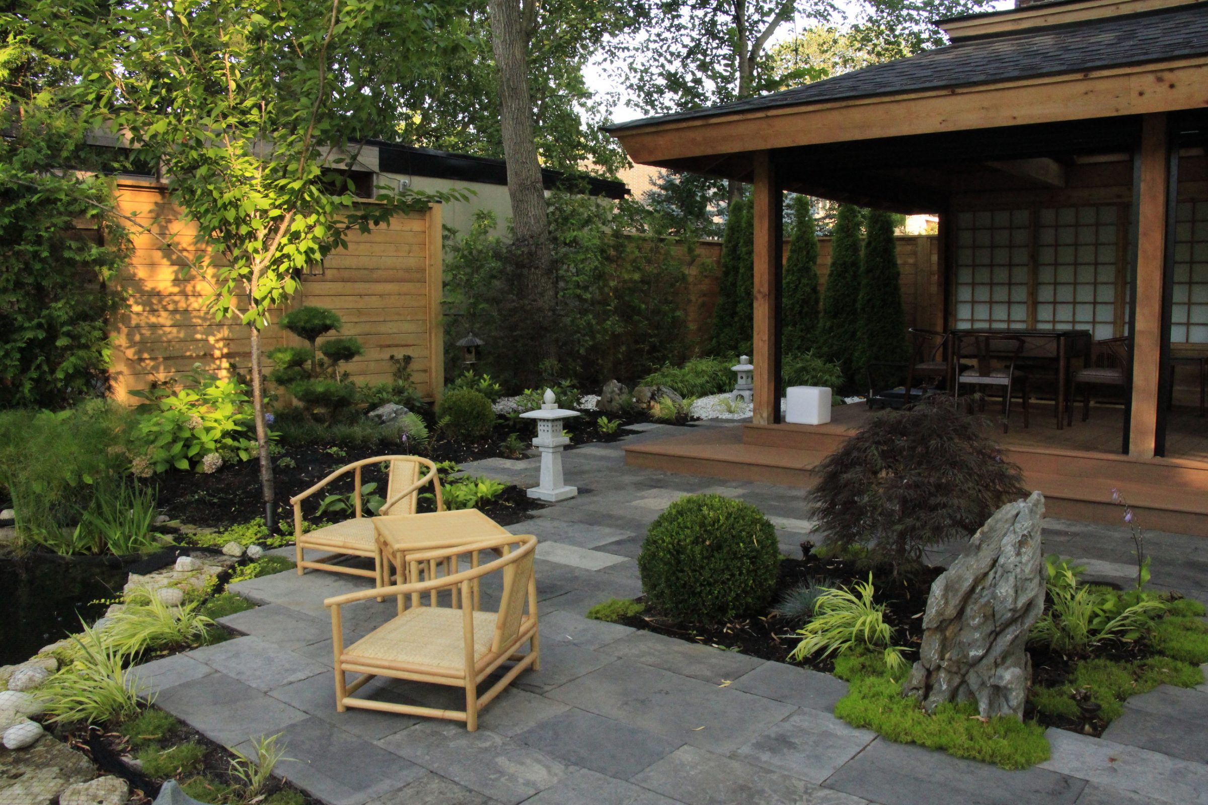 Serene Japanese garden with wooden patio and chairs.