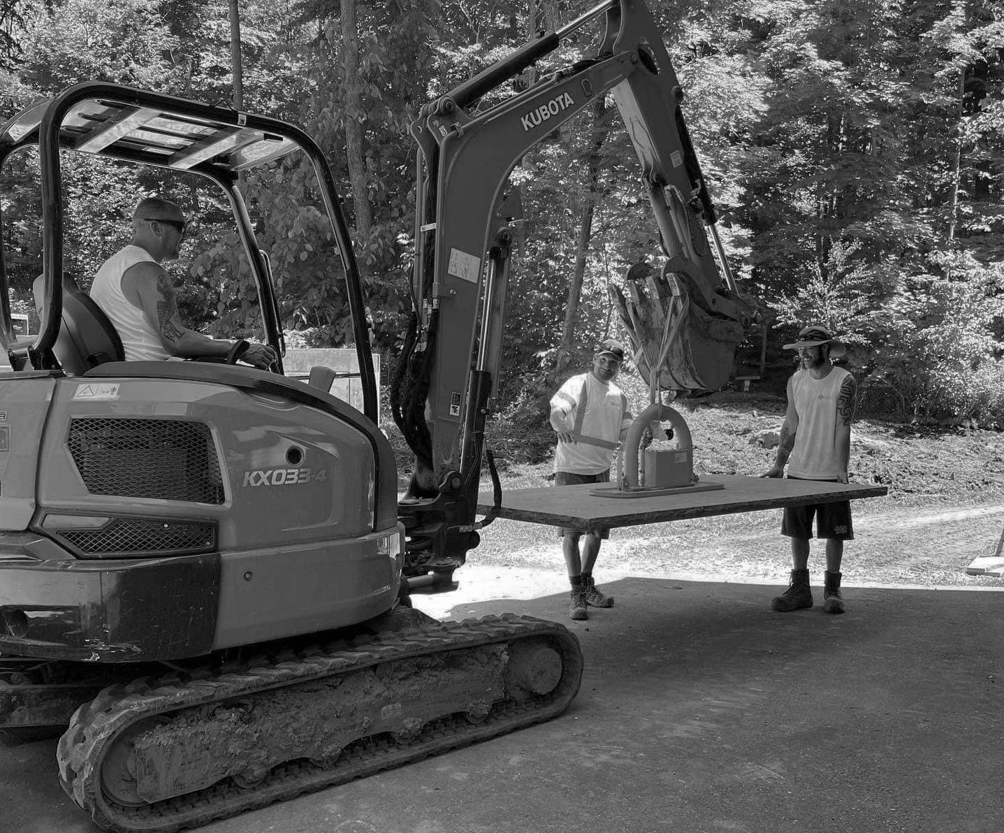 Workers using excavator to lift heavy equipment outdoors.