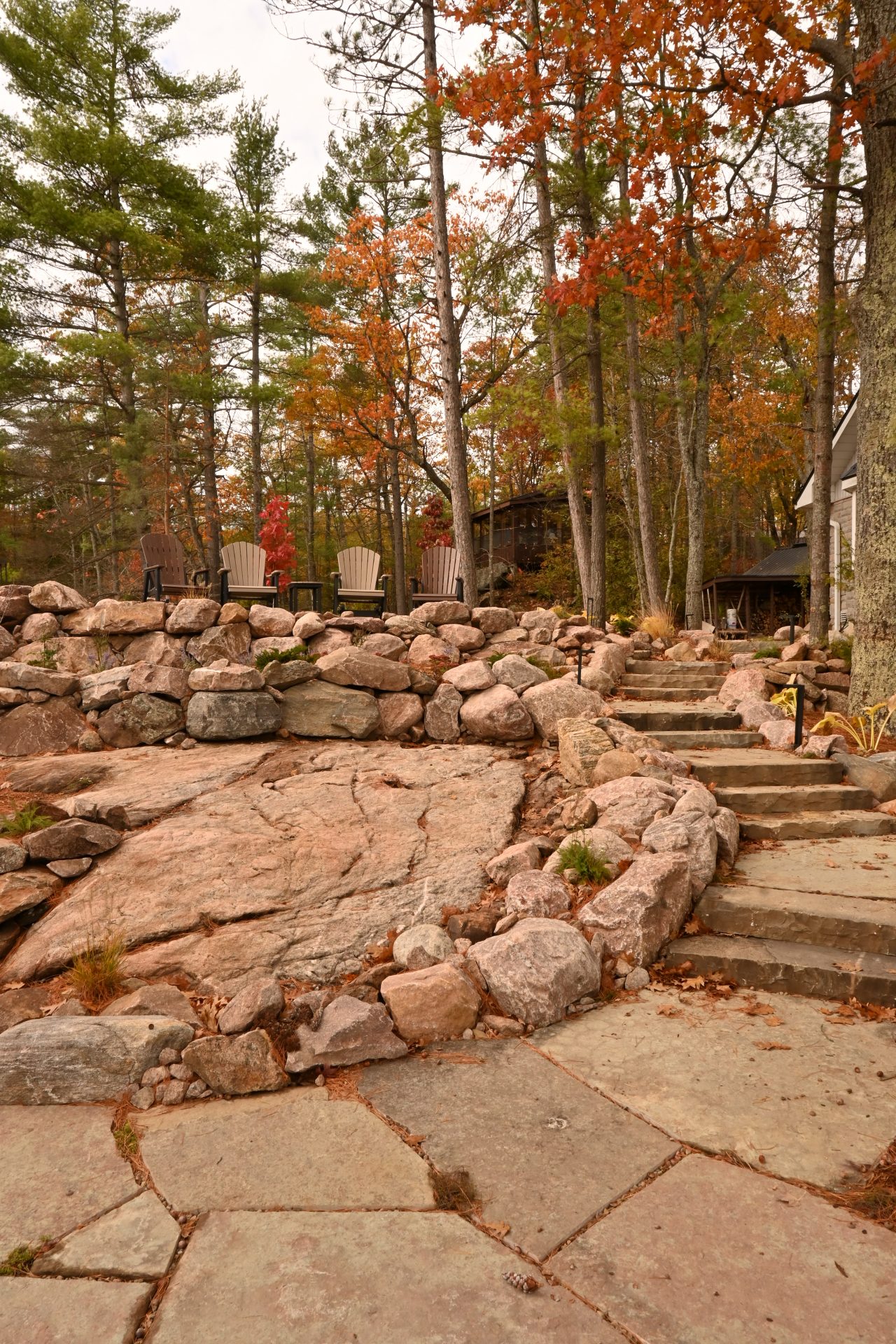 Rustic stone patio with Adirondack chairs in autumn forest.
