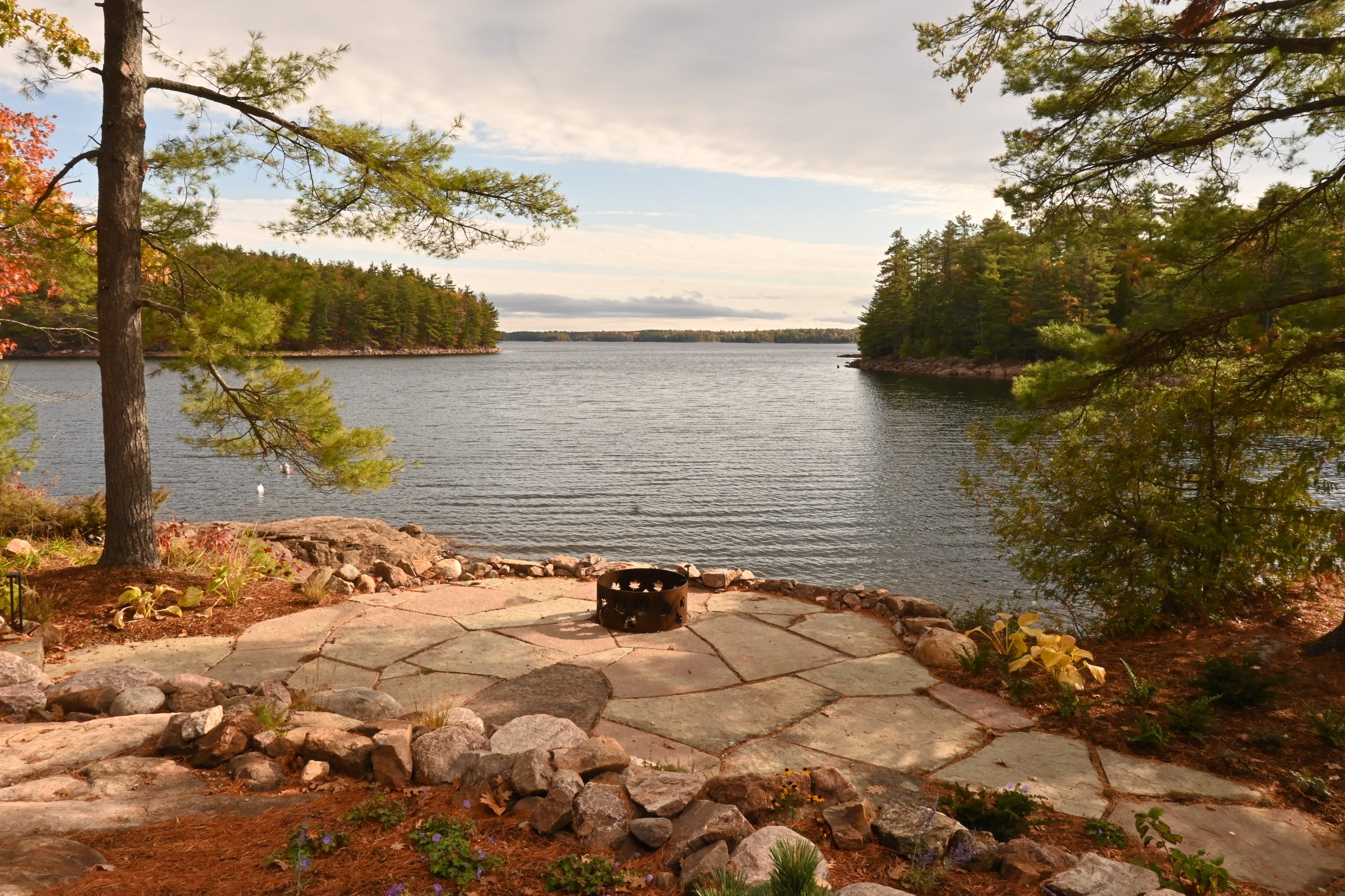 Lakeside fire pit with surrounding trees and rocks.