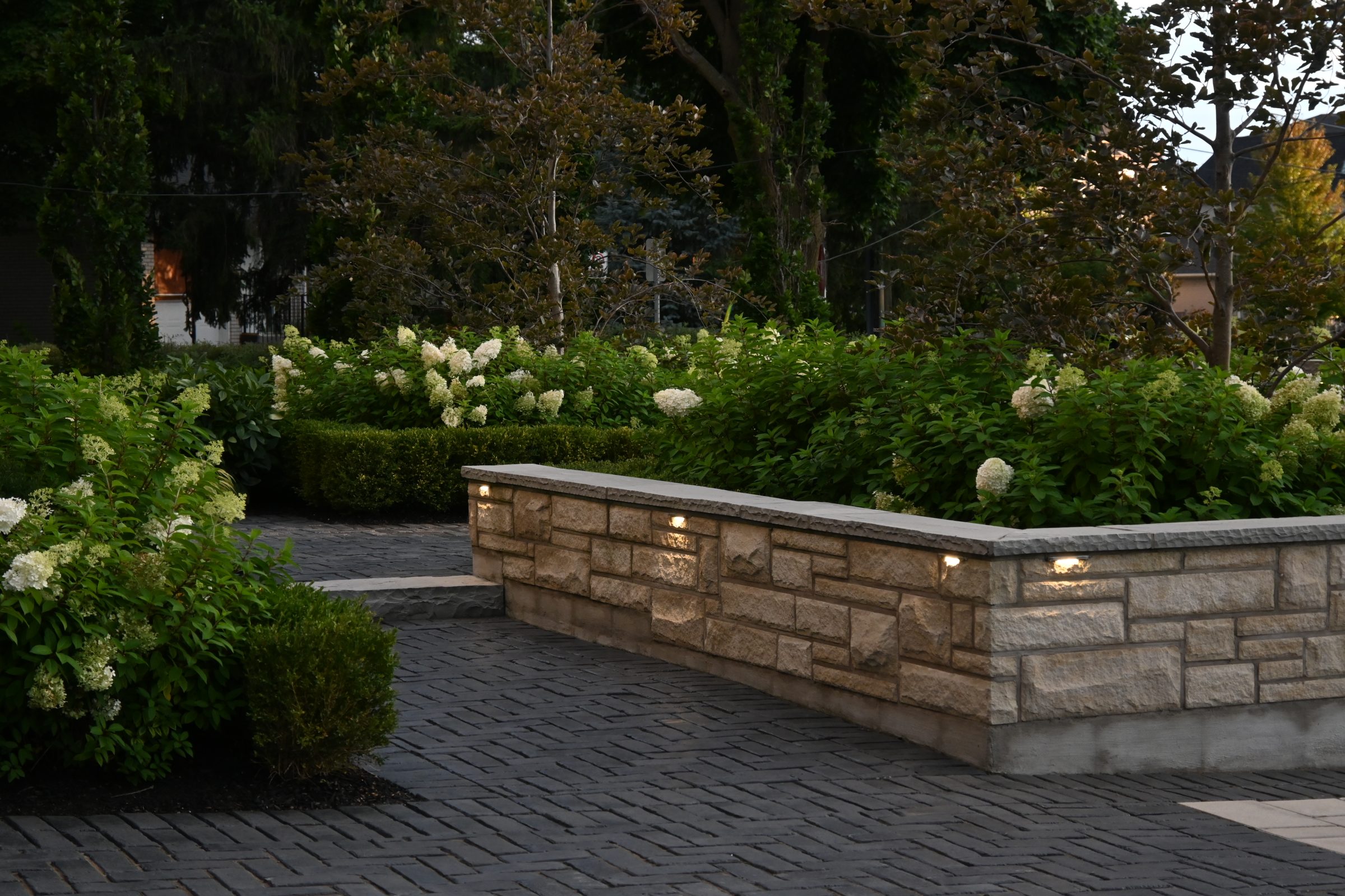 Illuminated garden walkway with stone wall and greenery.