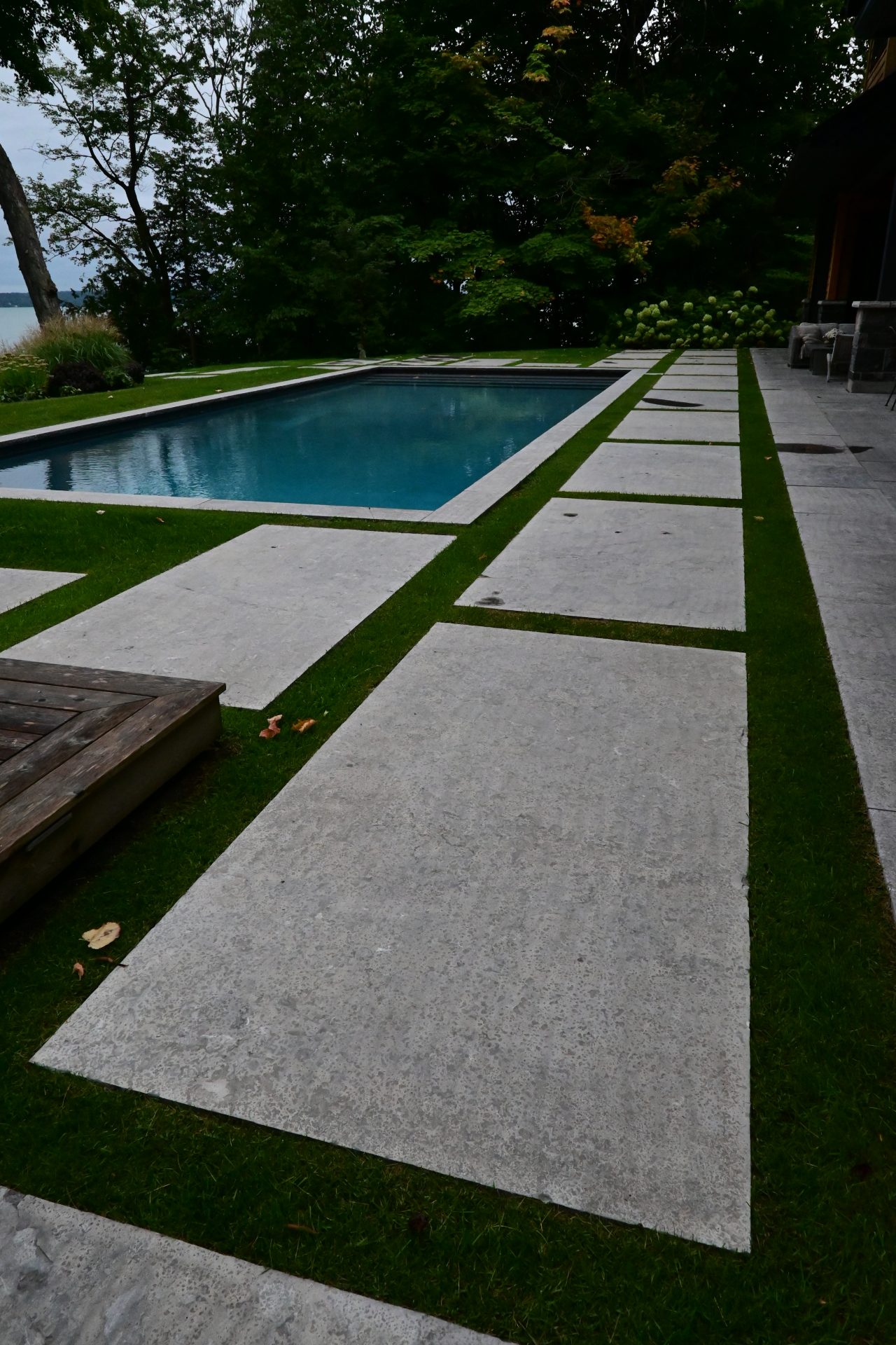 Modern backyard pool with stone walkway and trees.