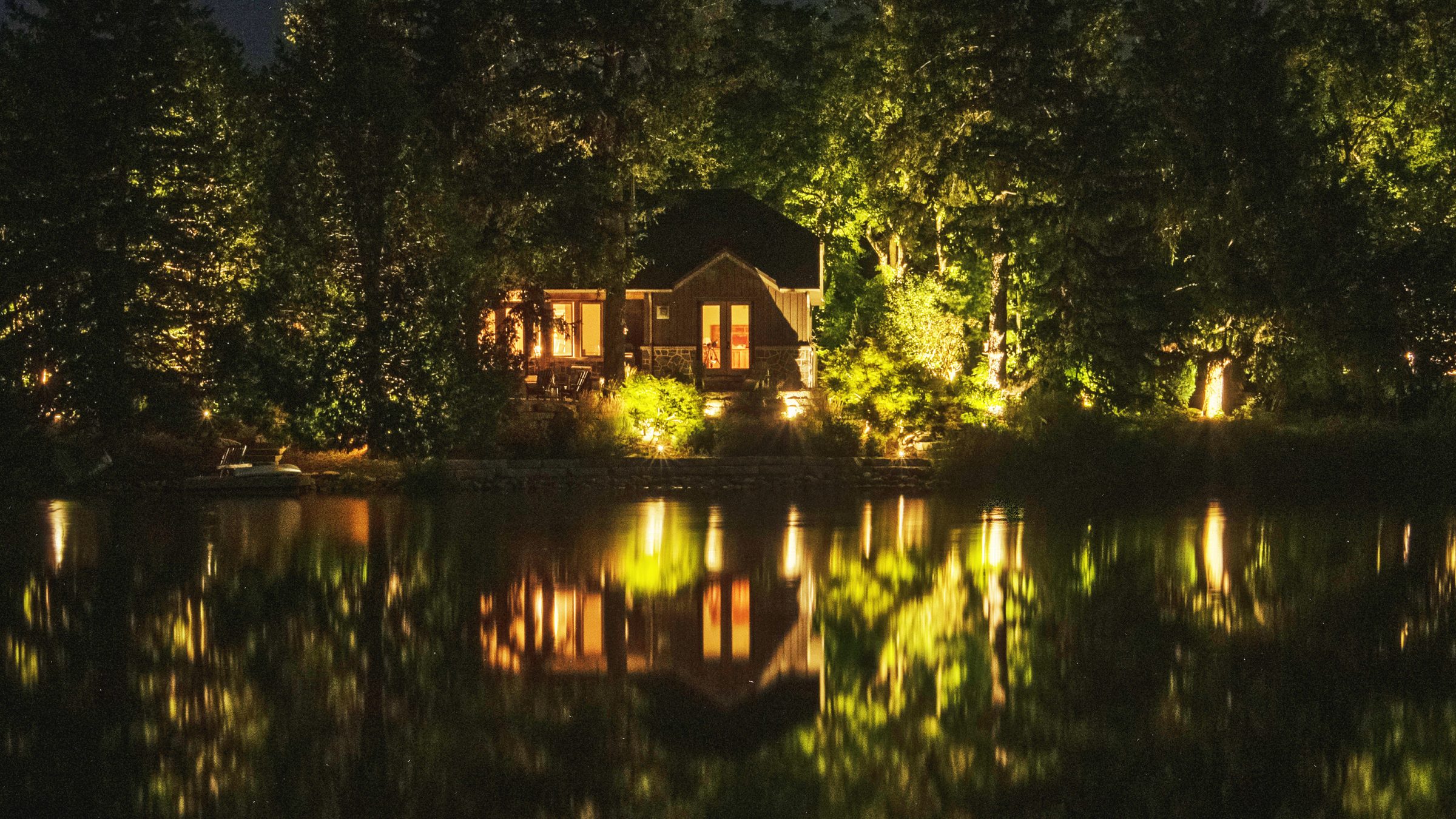House with lights reflecting on lake at night.