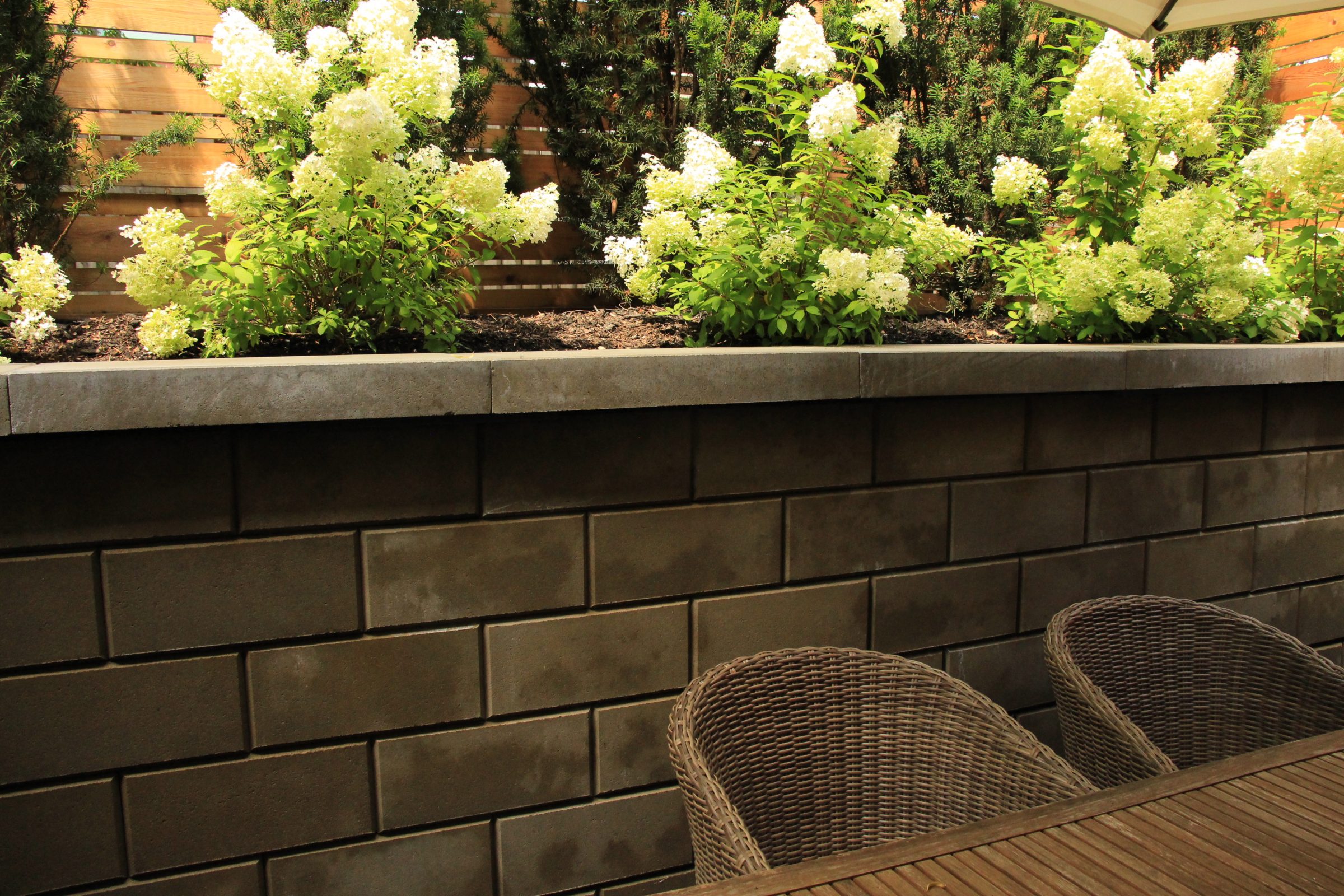 Patio furniture with flowering plants against brick wall.