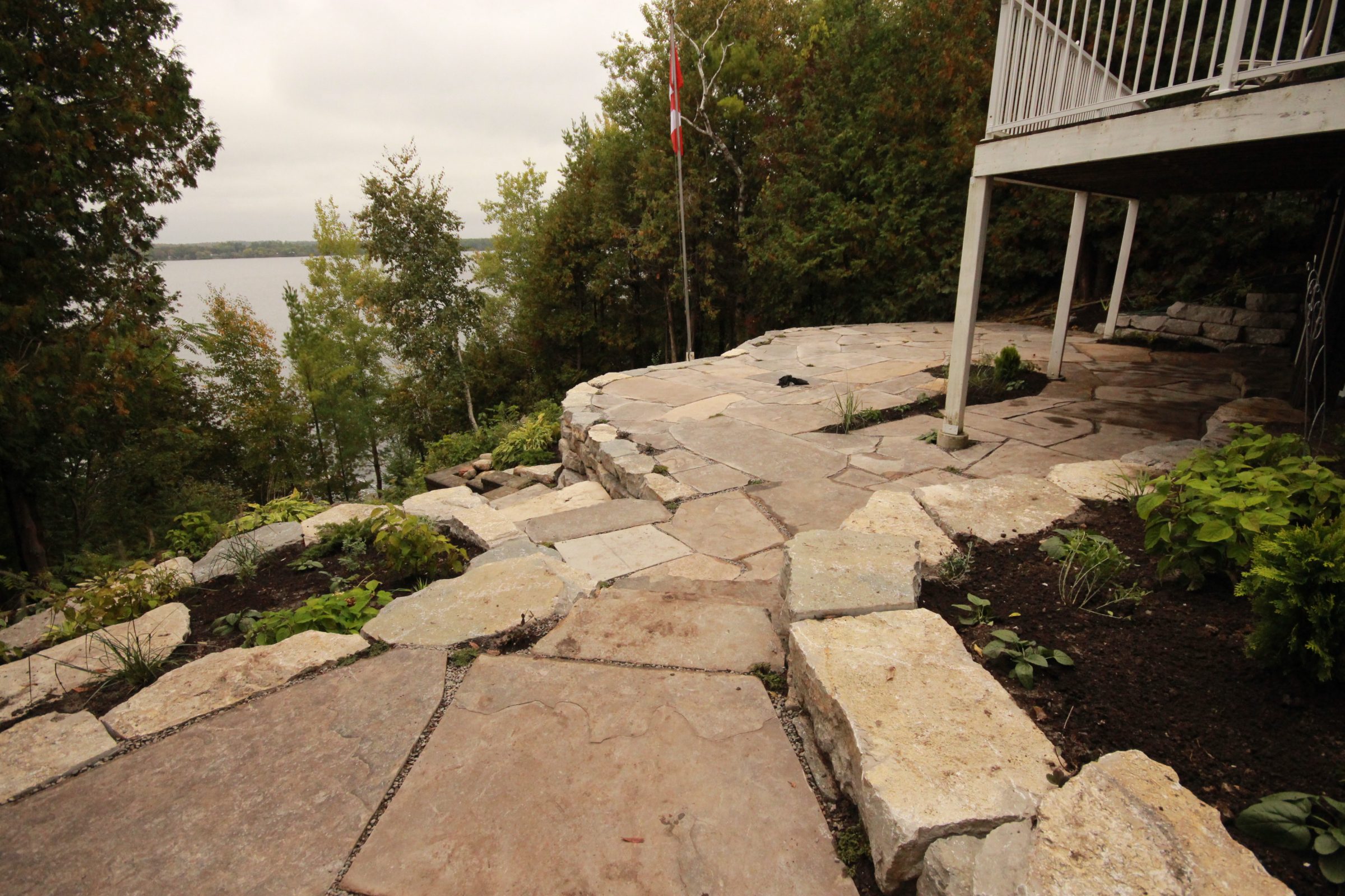 Lakeside stone patio with surrounding greenery and trees.