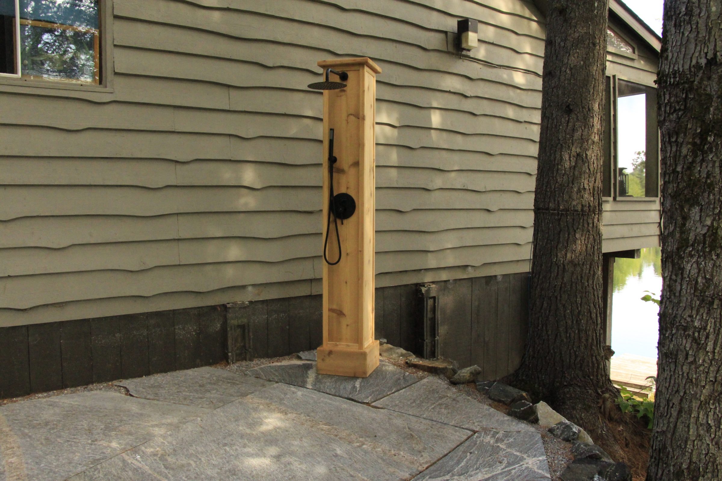Outdoor wooden shower beside house in forest setting.