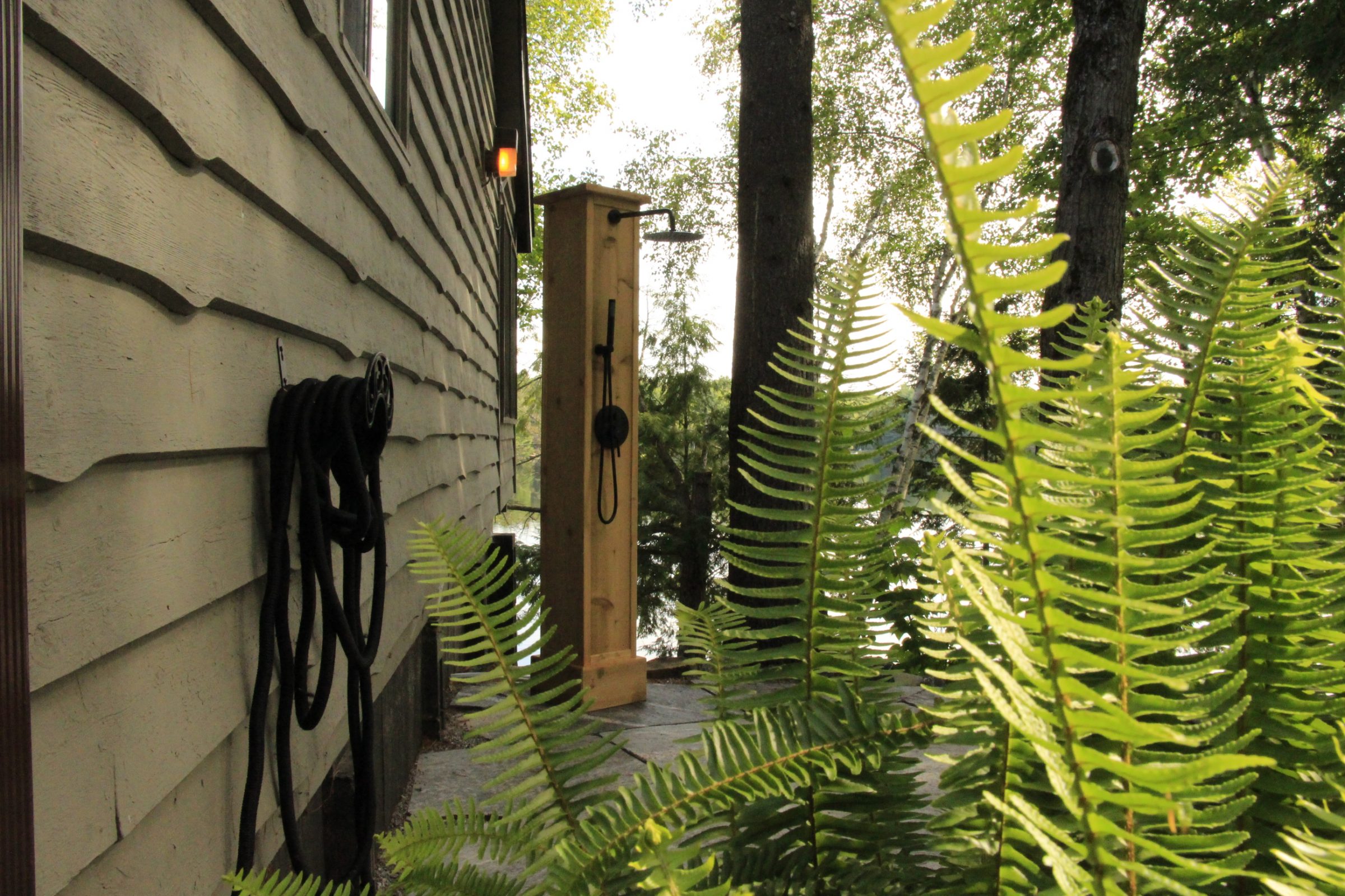 Outdoor shower near house with fern plants.