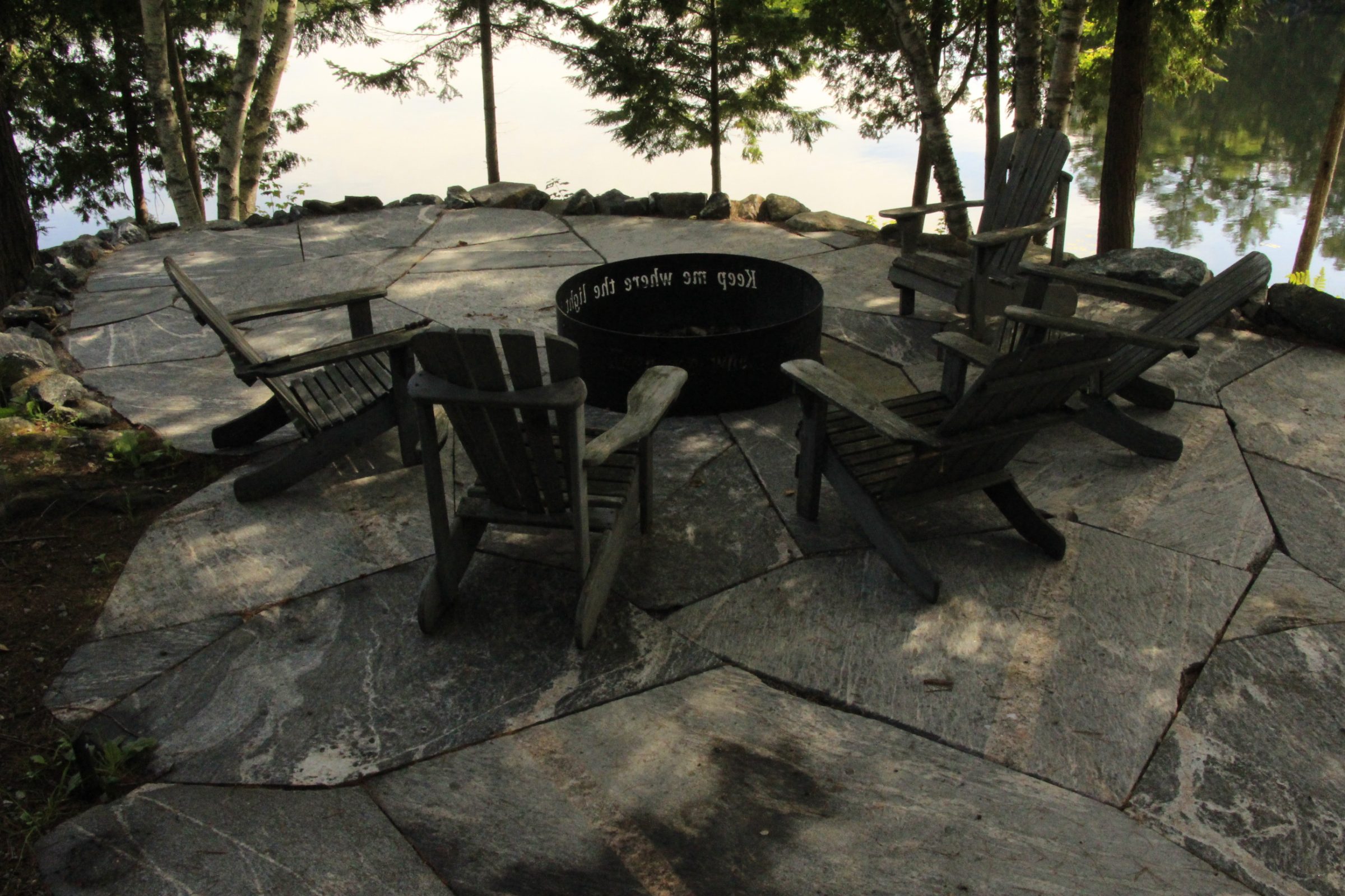Outdoor stone patio with Adirondack chairs and fire pit.