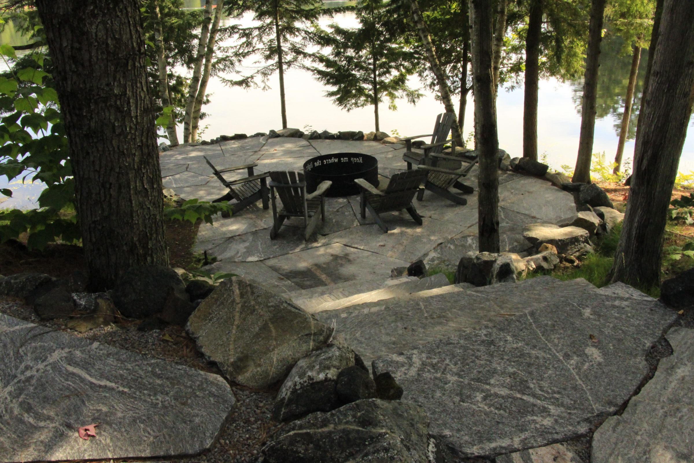 Stone patio with chairs by forested lake