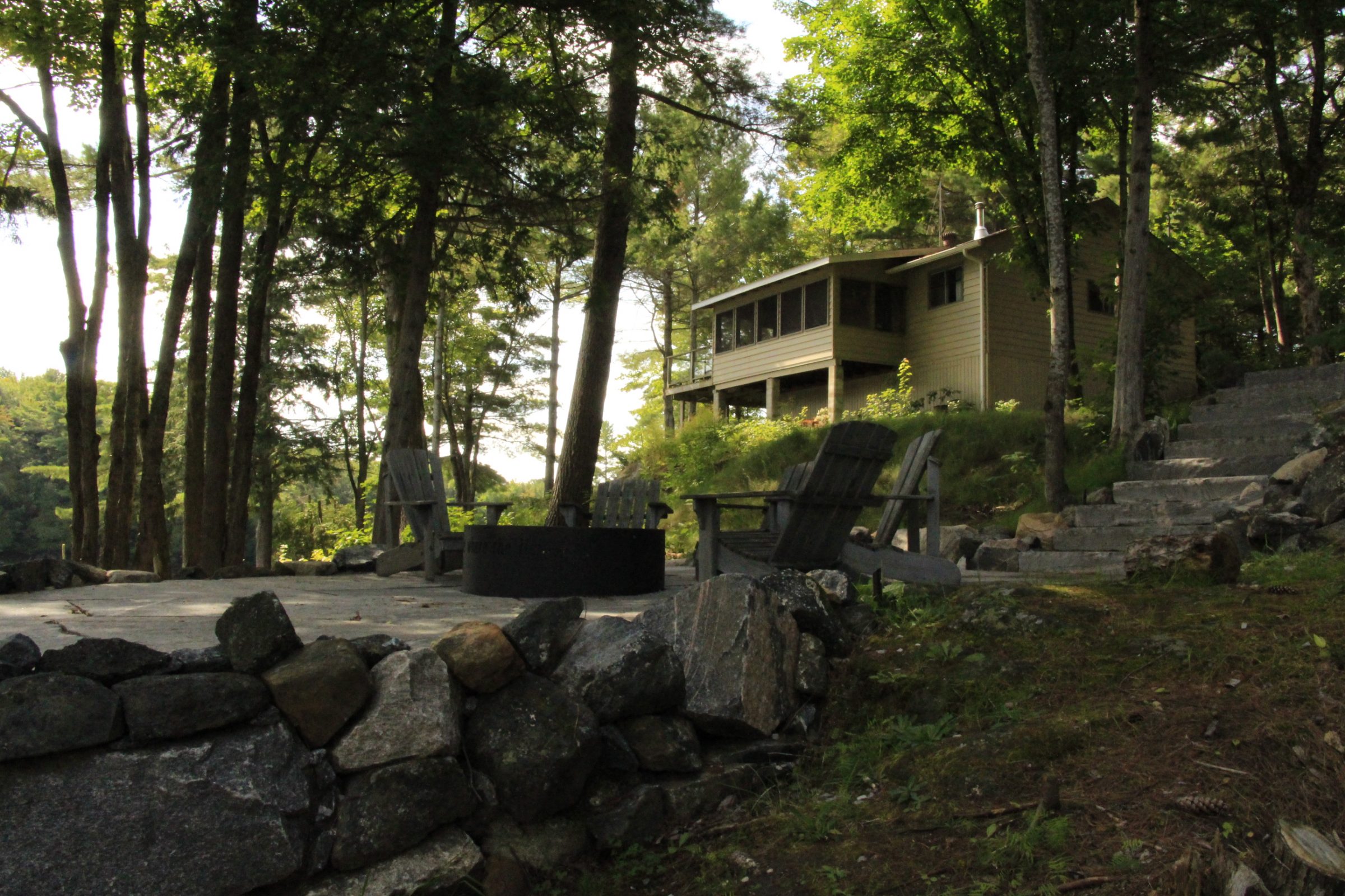 Rustic cabin with outdoor seating, surrounded by trees.