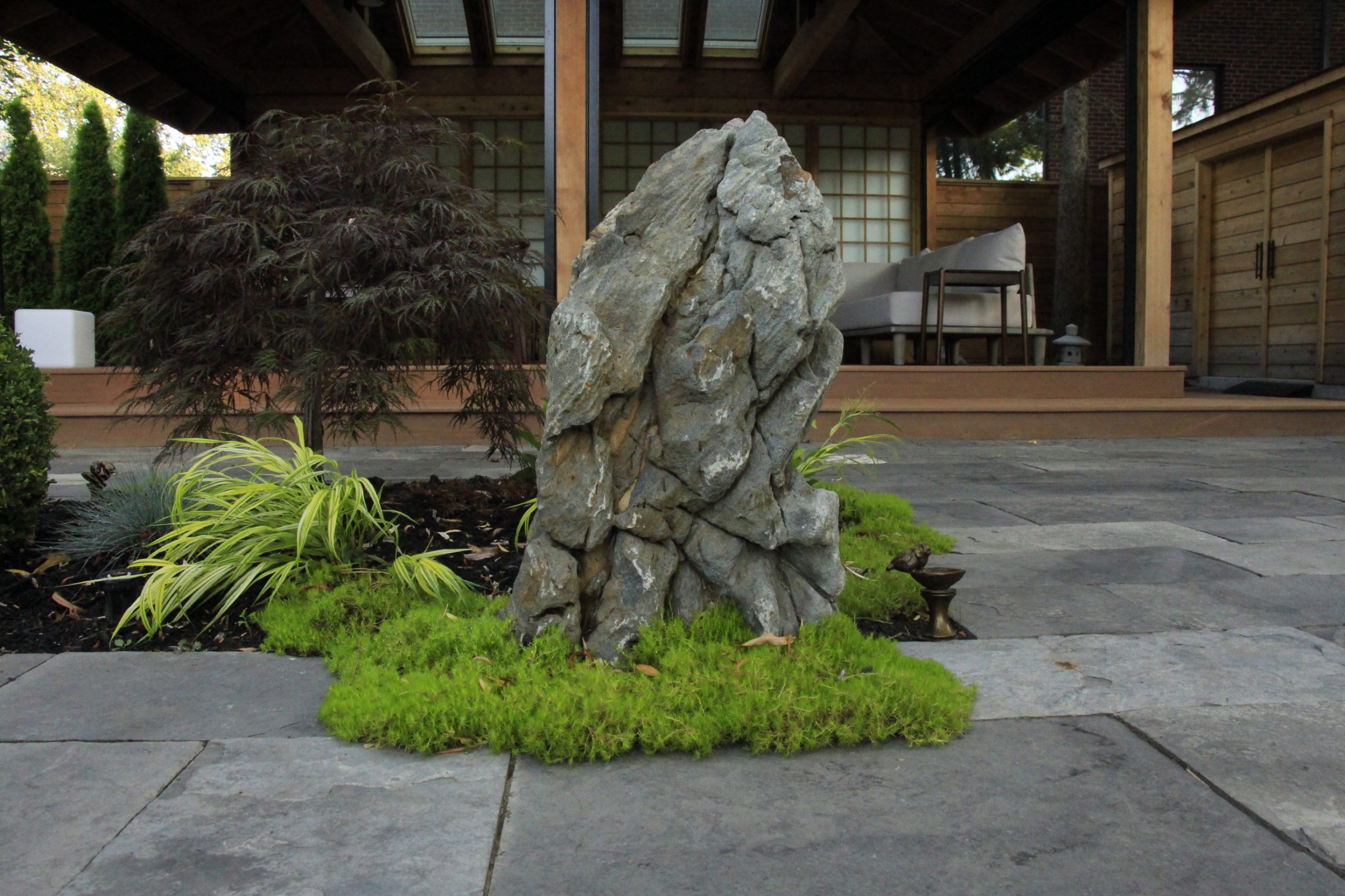 Rock garden with lush greenery and patio view.