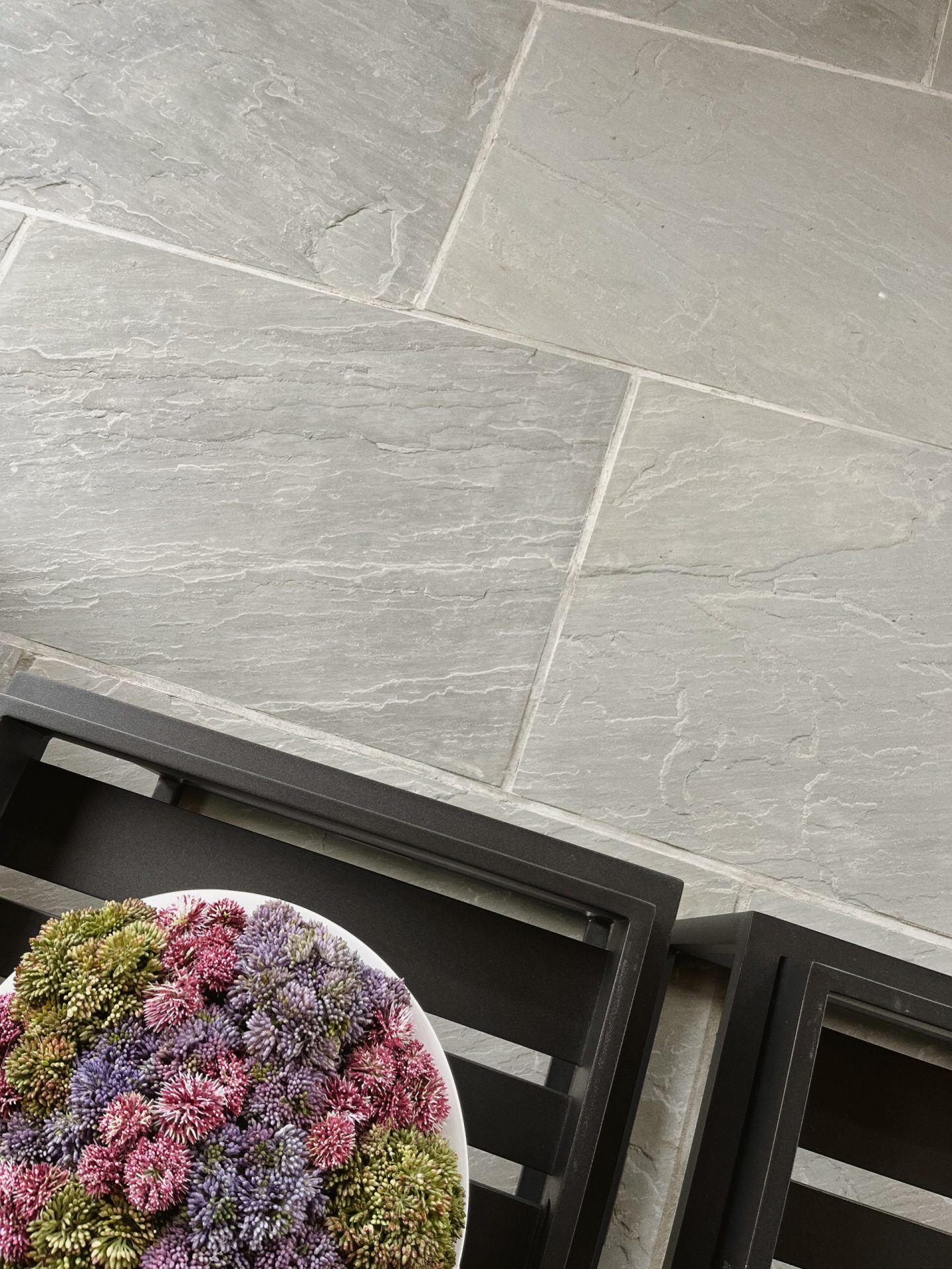 Colorful flowers on gray tiled floor with black chair.